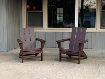 Two Adirondack chairs are placed side by side on a concrete patio in front of a windowed building