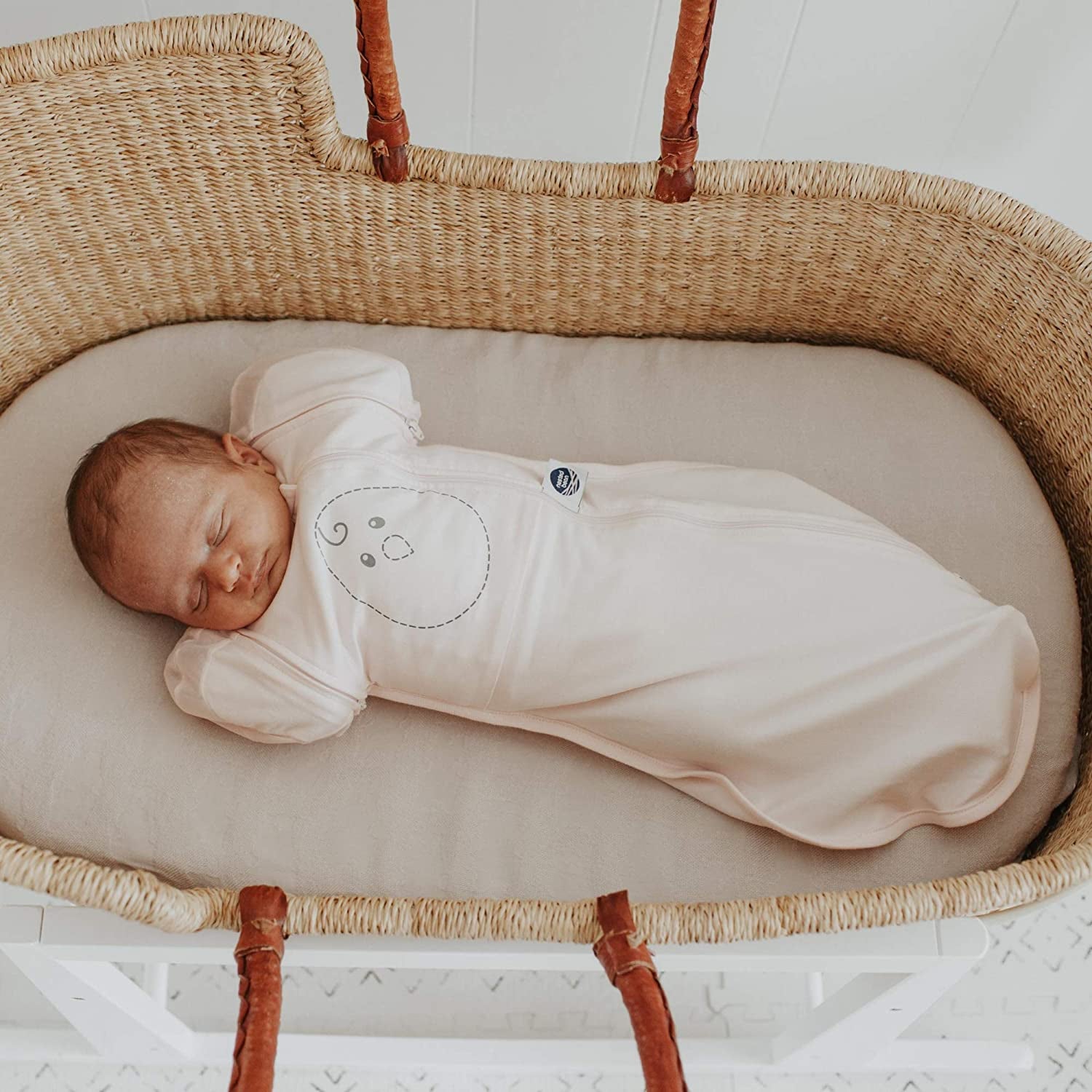 Model baby lying in bassinet with cream swaddle blanket 