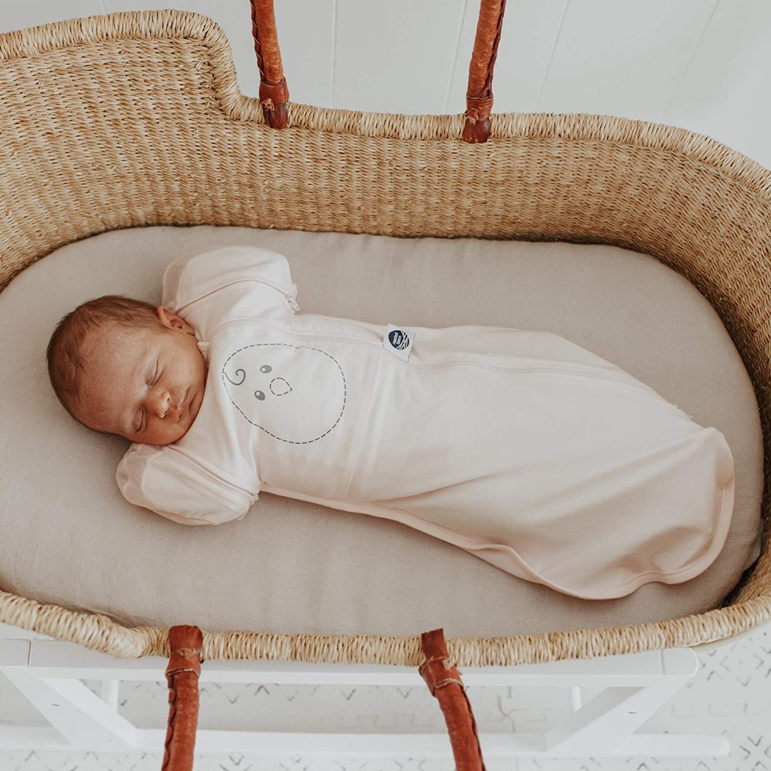 Model baby lying in bassinet with cream swaddle blanket