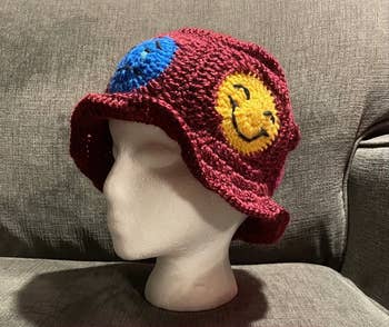 Burgundy crochet bucket hat with emojis along the side on a mannequin head 