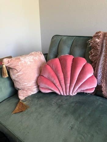 The seashell pillow in pink on a couch next to another pillow