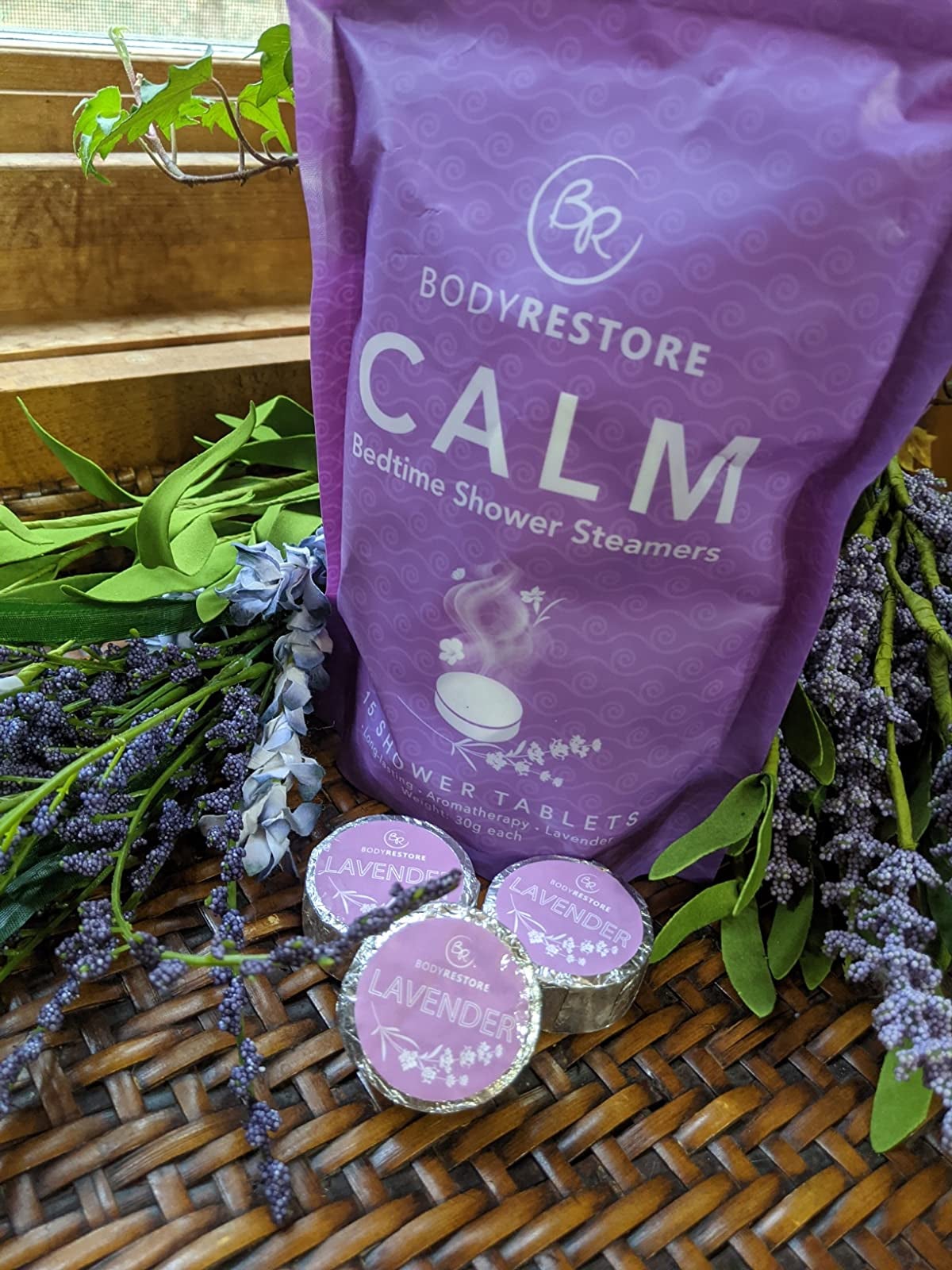 reviewer photo of three foil-wrapped lavender shower steamers in front of their package, surrounded by a lavender plant