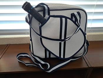 Tennis racket and white, perforated designer tennis bag with navy trim on a wooden surface