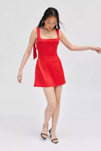 Person wearing a sleeveless, square-neck red dress and black sandals poses elegantly