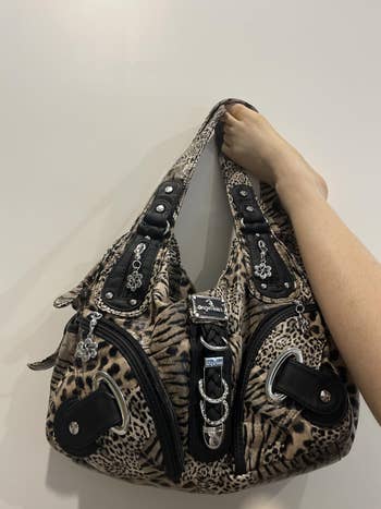 Person holding a stylish leopard-print handbag with decorative charms and shiny details