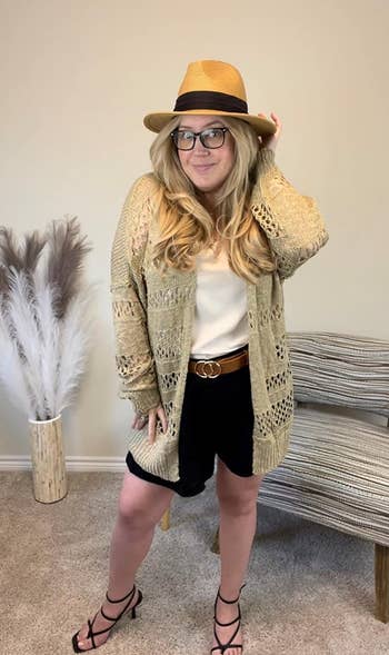 A reviewer wearing the cardigan in beige with shorts, heels, and a fedora