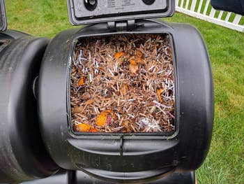 A compost bin filled with shredded paper, effect   peels, and integrated  waste, located outdoors connected  grass