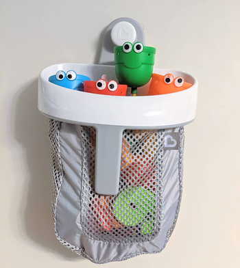 A mesh gray bag full of toys hung on a shower wall 