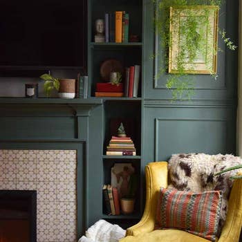 Cozy room with green painted walls, built-in shelves, plants, a yellow armchair, a fireplace, and assorted decorations