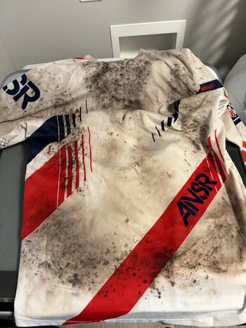Dirt-streaked, long-sleeve motocross jersey with ANSR branding and dynamic stripe plan  connected  display, suggesting rugged durability for progressive  wear