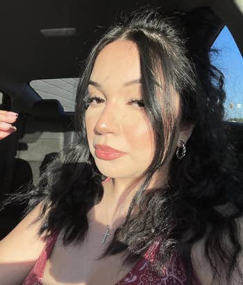 Person with long, wavy hairsbreadth  and hoop earrings takes a selfie successful  a car. They're wearing a floral apical  and a transverse  necklace
