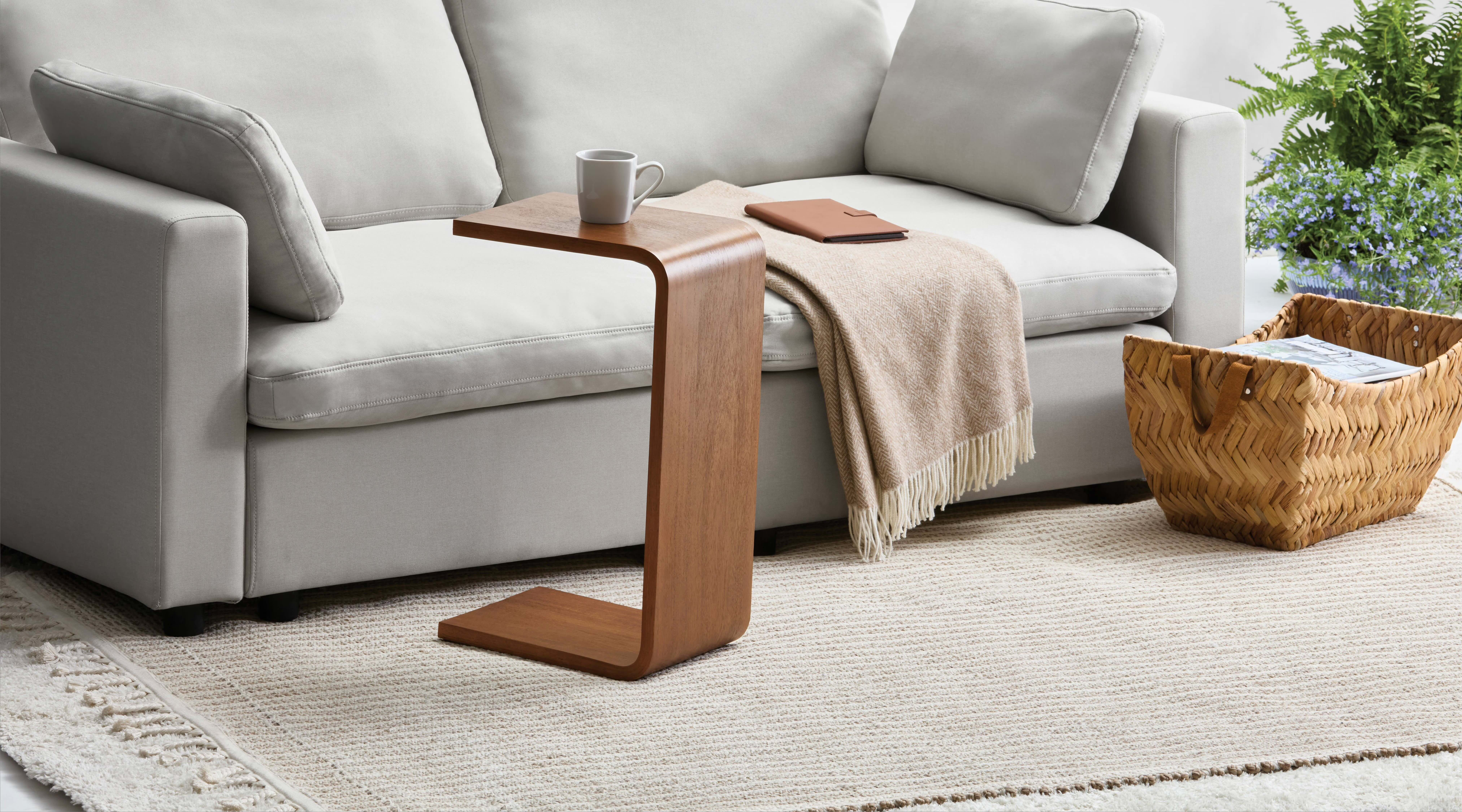 Modern surviving  country   with a sofa, cozy blanket, woody  C-shaped array  holding a mug, and a woven handbasket  connected  a textured rug