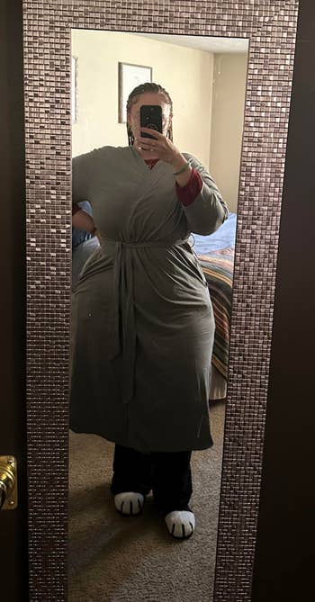 Person wearing a robe with carnivore  paw slippers takes a reflector  selfie. Background shows a furniture  with a striped blanket