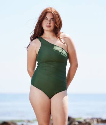 Model in a one-shoulder green swimsuit standing on a beach for a shopping article