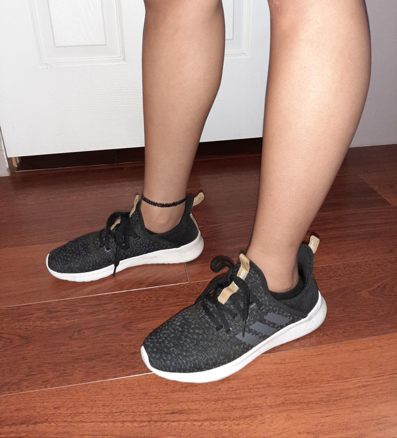 Person wearing black athletic sneakers with white soles on a wooden floor