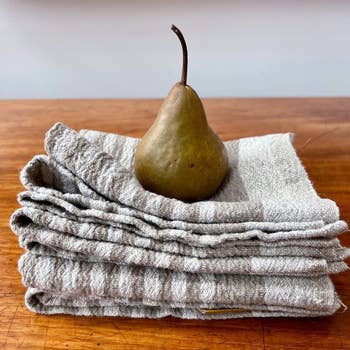 A fresh pear rests on a stack of folded linen tea towels