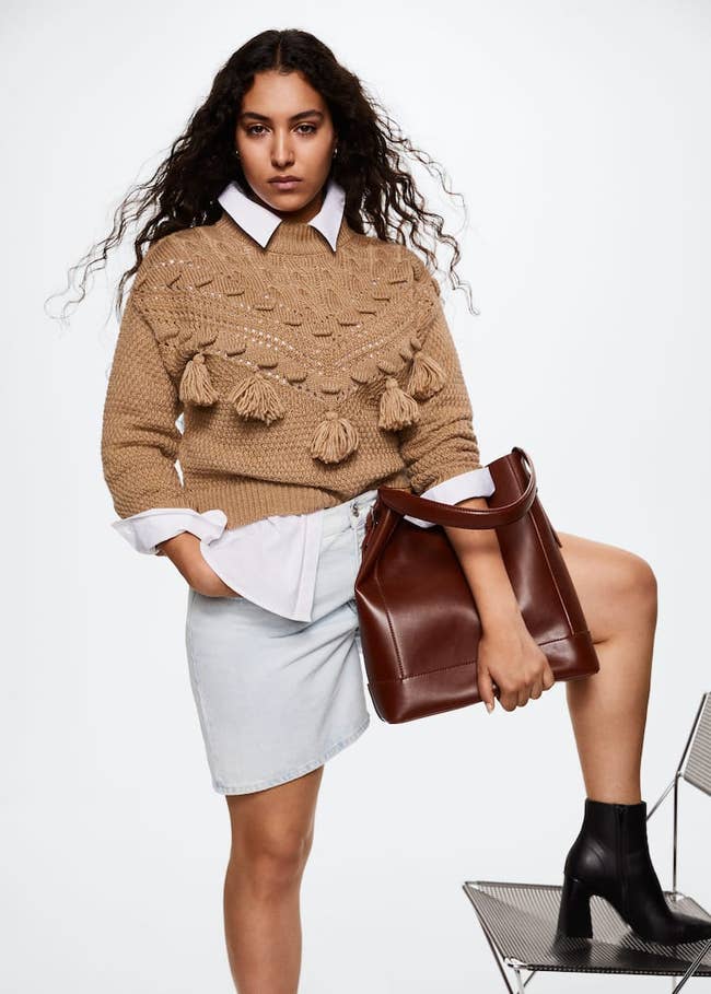 a model posing in the tan sweater with four pompoms in front 
