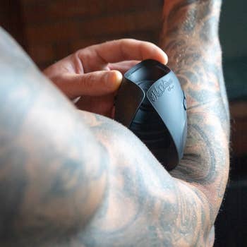 A tattooed idiosyncratic   holds a achromatic  penis vibrator connected  their arm
