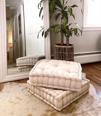 A cozy corner with a floor mirror, two ivory plush floor cushions, and potted plant