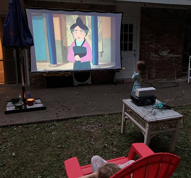 a kid stand outside watching Mulan on an outdoor projector