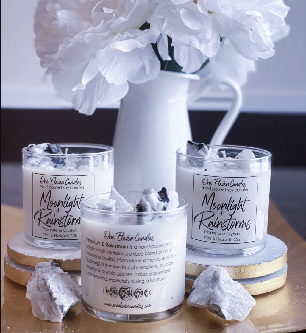 Three candles are displayed next to crystals and a vase filled with white flowers