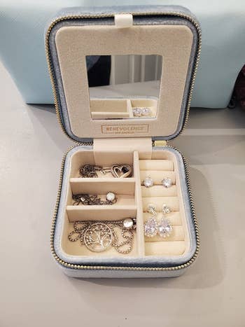 reviewer photo of the jewelry organizer holding three necklaces and two pairs of earrings