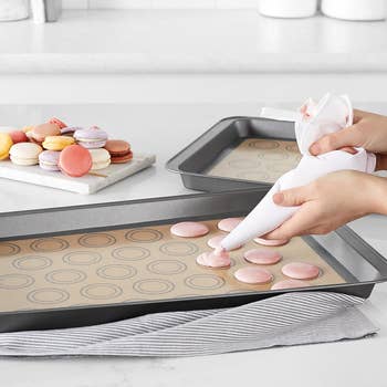 someone using a piping bag on a silicone baking mat with pre-measured circles on it