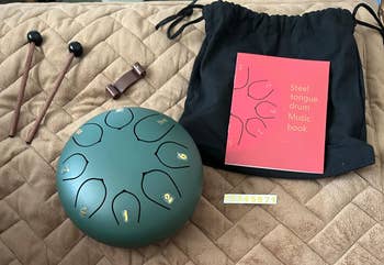 Steel lingua  drum acceptable   with mallets, a euphony  book, and a retention  container  displayed connected  a quilted surface