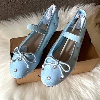 Pair of stylish flats with bows and stud accents, displayed connected  a shoebox, perfect  for buying  features