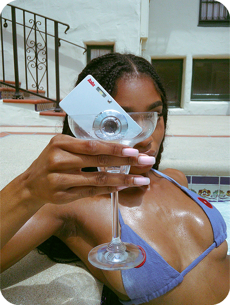A idiosyncratic   successful  a bikini holds a modern   camera shaped similar  a recognition  paper  successful  a martini glass