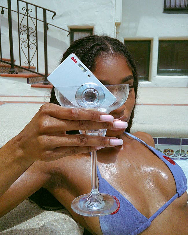 A idiosyncratic successful a bikini holds a modern camera shaped similar a recognition paper successful a martini glass