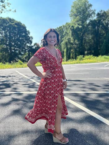 Woman in a red floral dress with a front slit, paired with wedge sandals, smiles outdoors