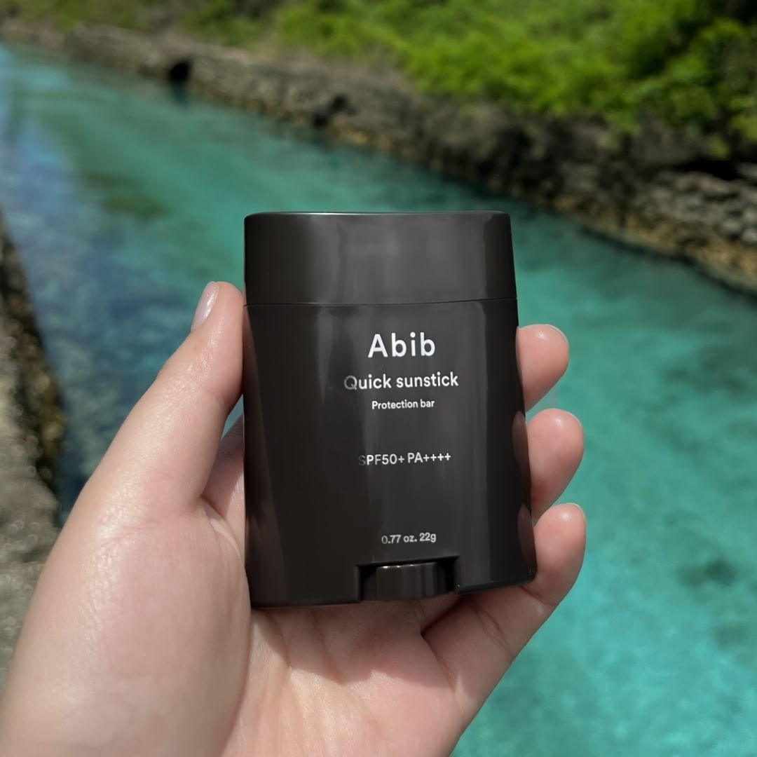 model holding an Abib Quick Sunstick SPF50+ product with a river in the background