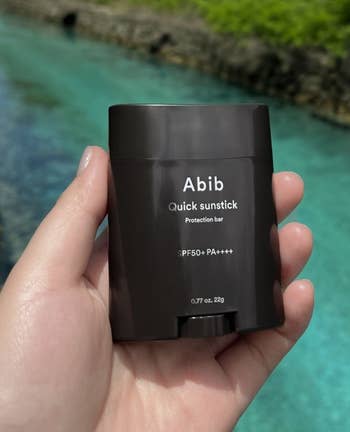 model holding an Abib Quick Sunstick SPF50+ product with a river in the background