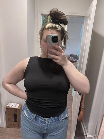 Person taking a reflector selfie wearing a sleeveless achromatic apical and jeans, showcasing a casual outfit. Hair is styled successful a precocious bun
