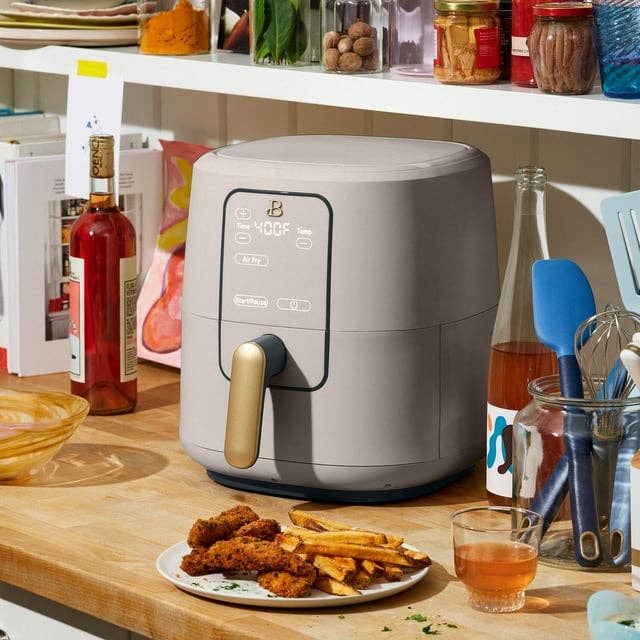 Countertop air fryer with display, next to plate of fried food, positioned in a home kitchen setting for product showcase
