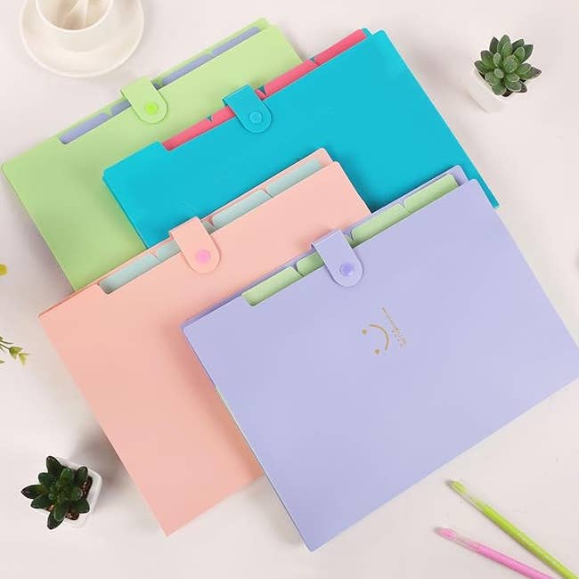 four folded accordion files in purple, pink, blue and green