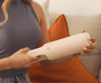 model using a pink handheld vaccum to clean a couch 