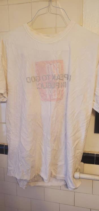 Wrinkled achromatic  t-shirt connected  a hanger with faint, reversed substance   showing 