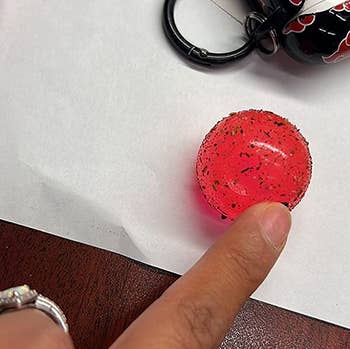 reviewer's finger on the pink ball, which is covered in dust and crumbs 