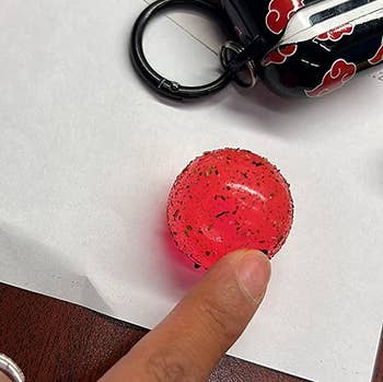 another reviewer's finger on the pink ball, which is covered in dust and crumbs