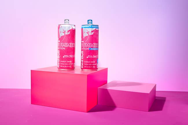 Two cans of Red Bull Summer Edition vigor  portion  displayed connected  pinkish  podiums against a pinkish  backdrop