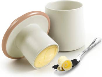 Butter in a mushroom shaped ramekin with lid, next to a curl of butter on a spoon 