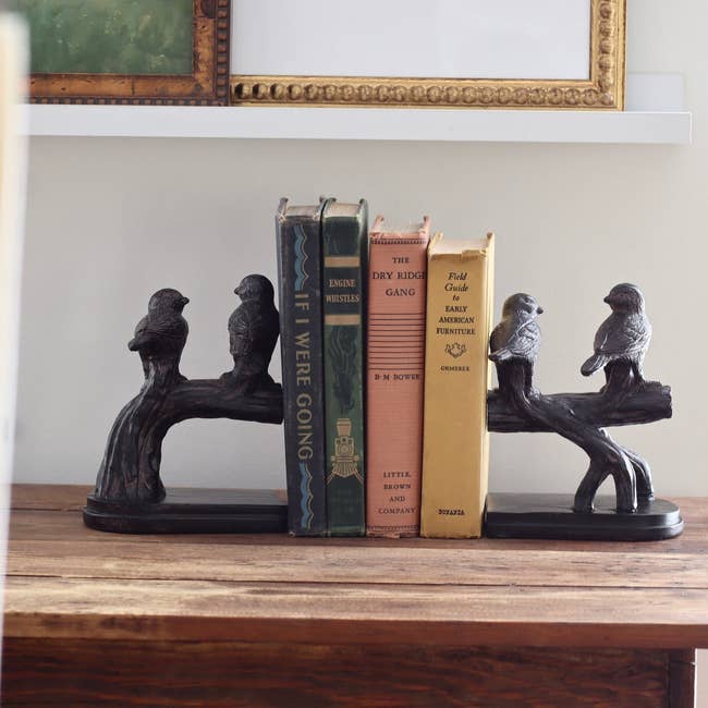 two bookends shaped like two birds on a branch holding a stack of three books