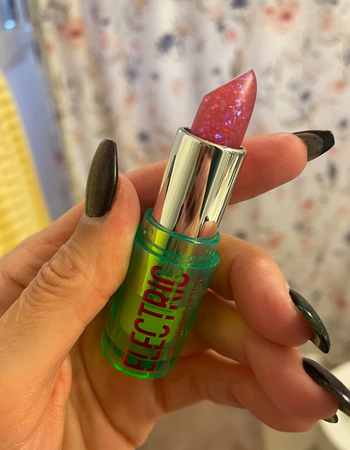 Reviewer holding up pink clear glittery lipstick