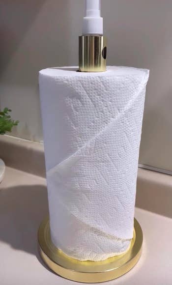A gold paper towel roll with a spray bottle sticking out from the middle 