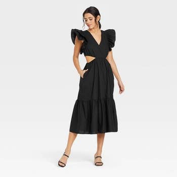 model in black sleeveless dress with large ruffles at shoulders and cutouts at waist