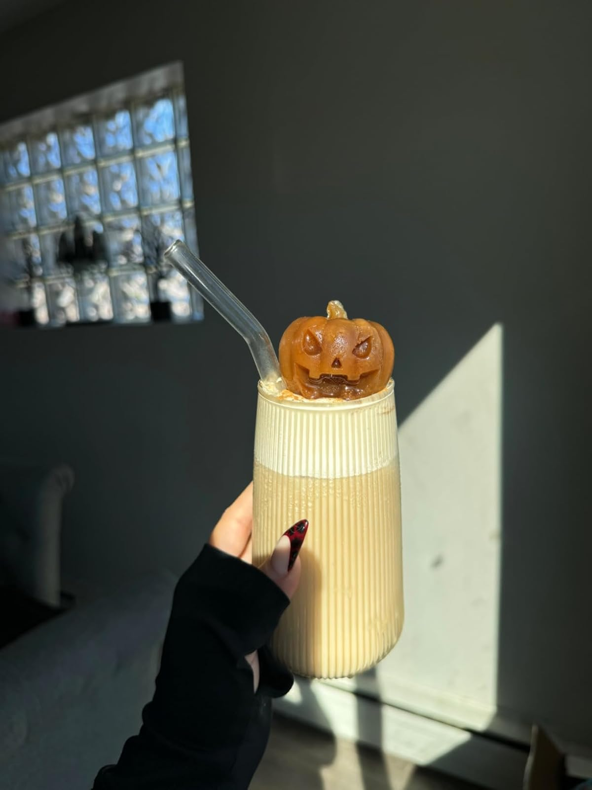 Person holding a glass with iced coffee, topped with a small pumpkin decoration and a clear straw.