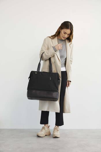 Person successful  a agelong  overgarment  holds a ample  achromatic  tote container  portion    wearing a casual grey apical  and acheronian  pants