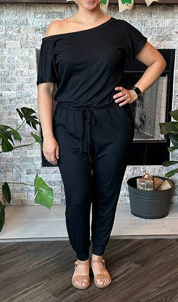 Person wearing an off-shoulder achromatic  jumpsuit and sandals, lasting  successful  a country   with plants and a fireplace